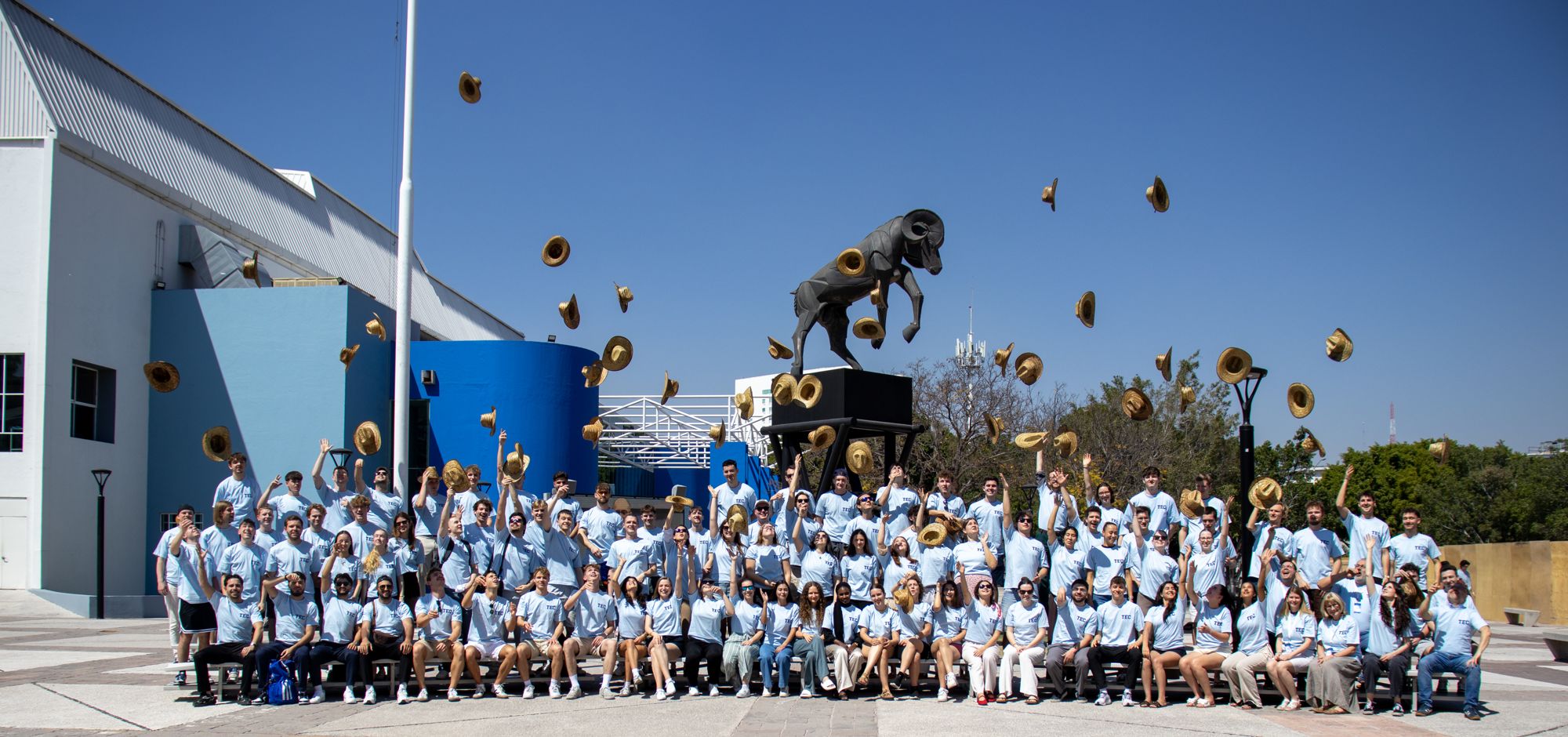 Gruppenfoto der Winterschool-Teilnehmenden in hellblauen T-Shirts, die ihre Strohhüte in die Luft werfen